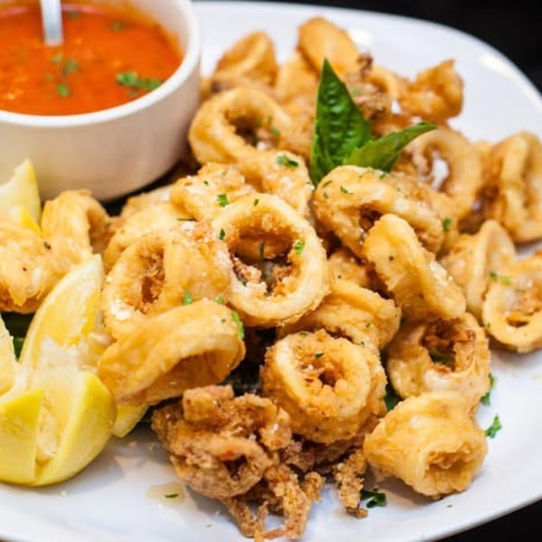 Crispy fried calamari with lemon wedges, fresh basil, and a side of marinara sauce.