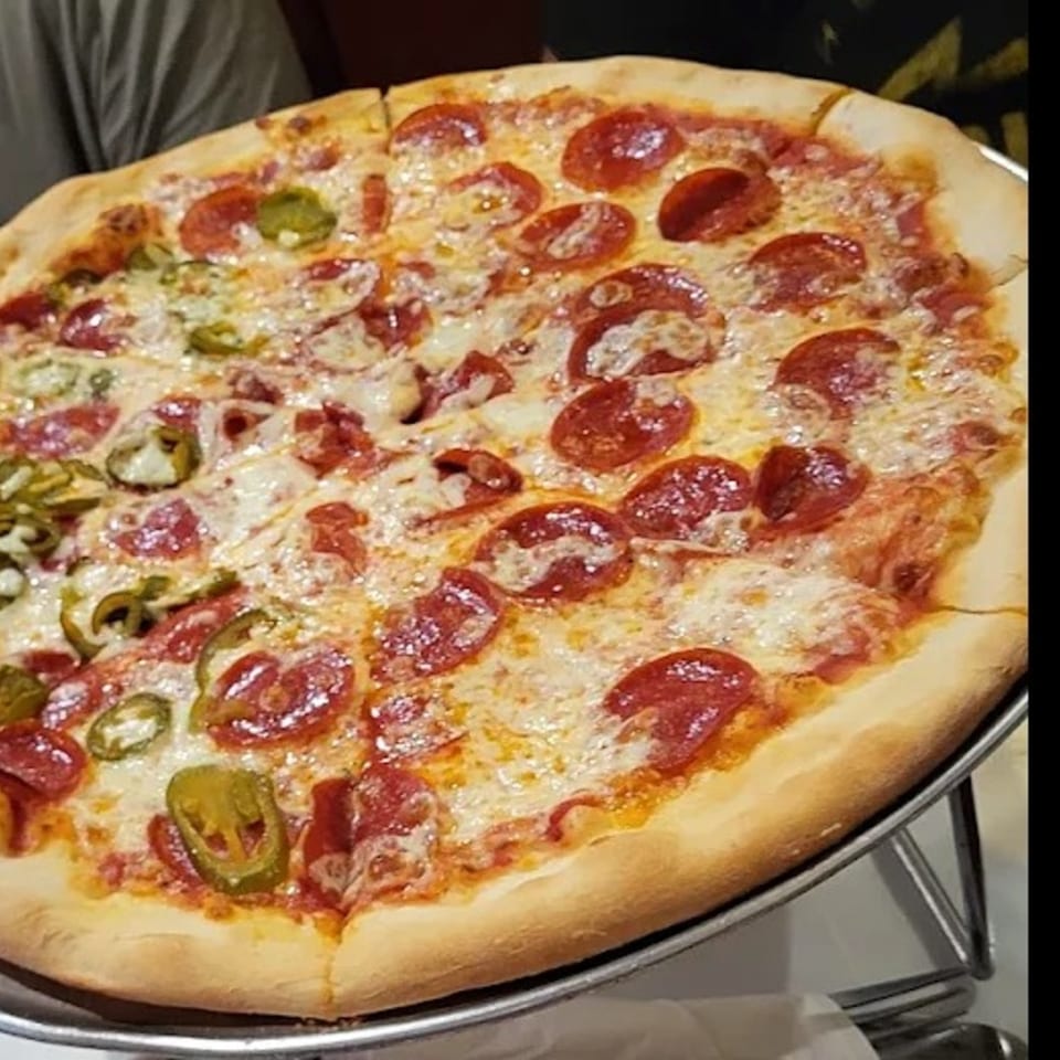 A large, round pizza with pepperoni and jalapeños on a metal stand.