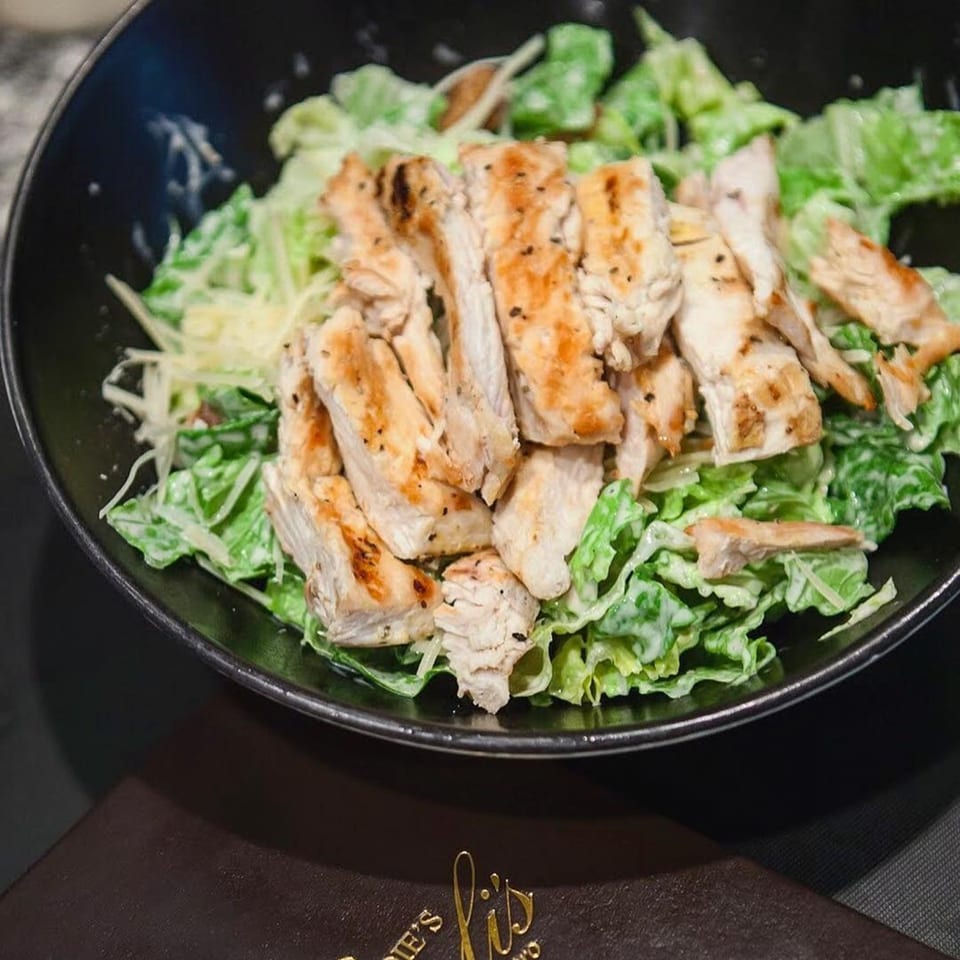 Grilled chicken Caesar salad with crisp romaine lettuce and creamy dressing in a black bowl.