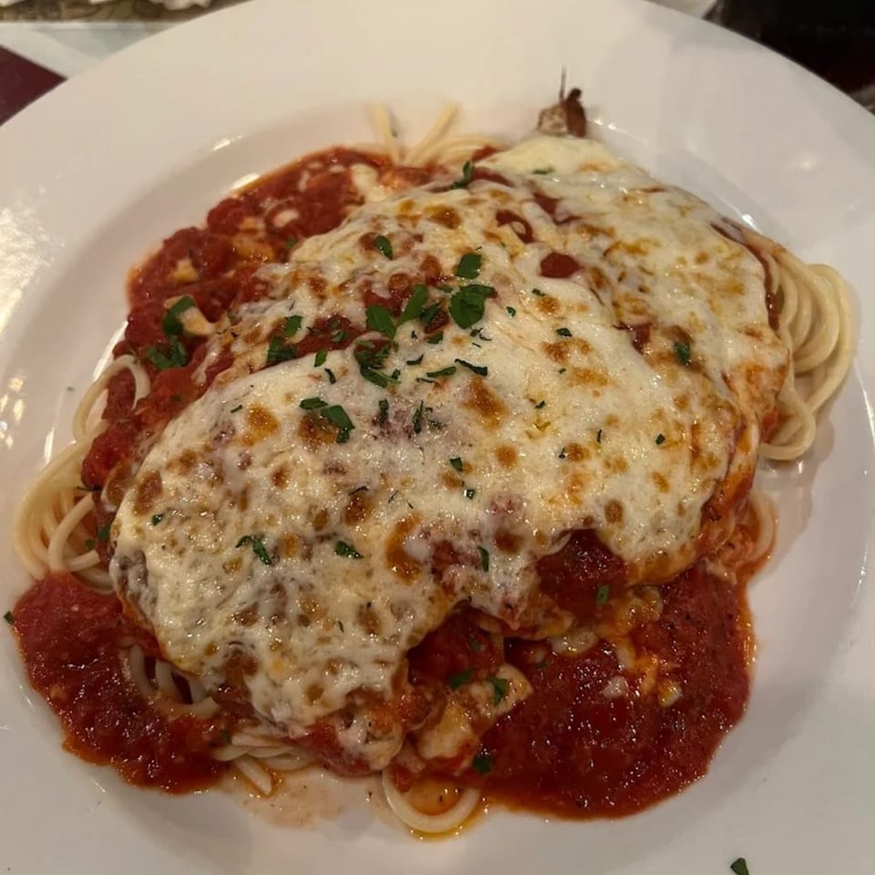 Chicken Parmesan with melted mozzarella cheese and red sauce over spaghetti on a white plate.