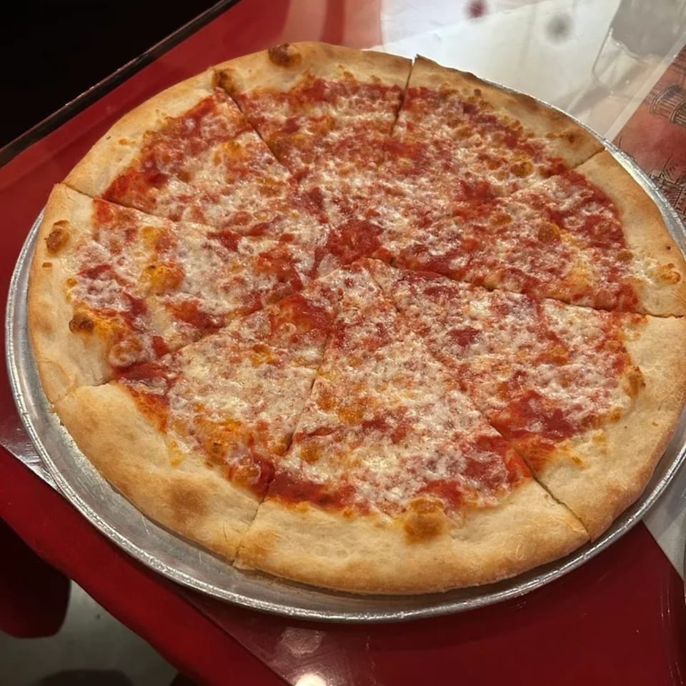 A whole, sliced cheese pizza with red sauce on a metal pan, on a red table.