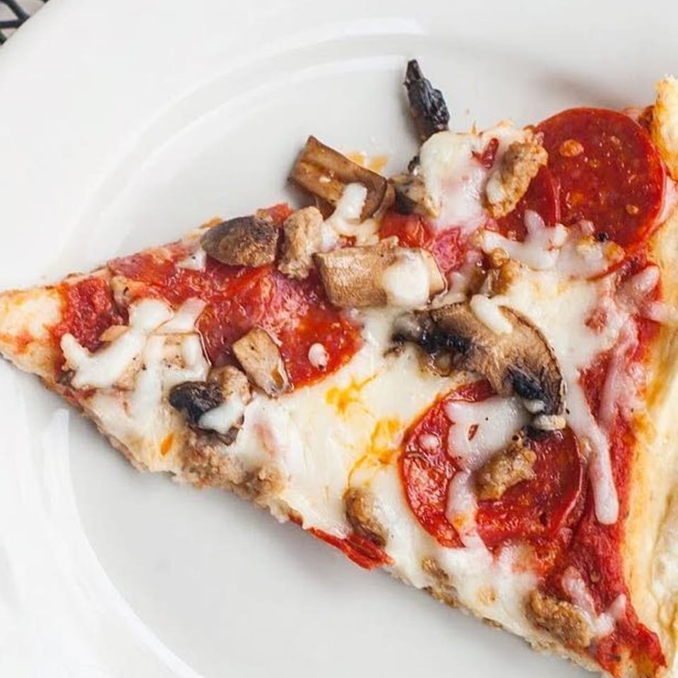 A slice of Eddie's Napolis Italian Bistro pizza with pepperoni, sausage, and mushrooms.
