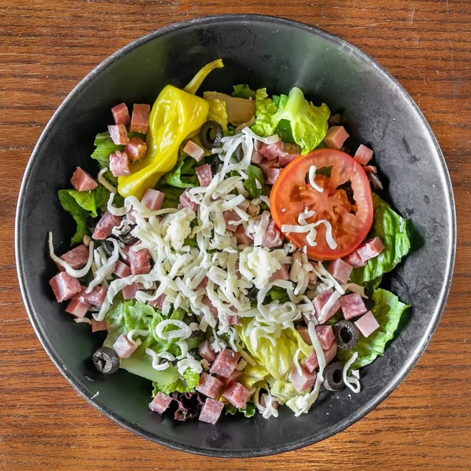 Overhead view of a fresh Italian salad with lettuce, ham, cheese, olives, tomato, and pepperoncini.